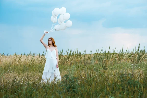 Selective focus of redhead girl holding balloons in grassy field — Stock Photo