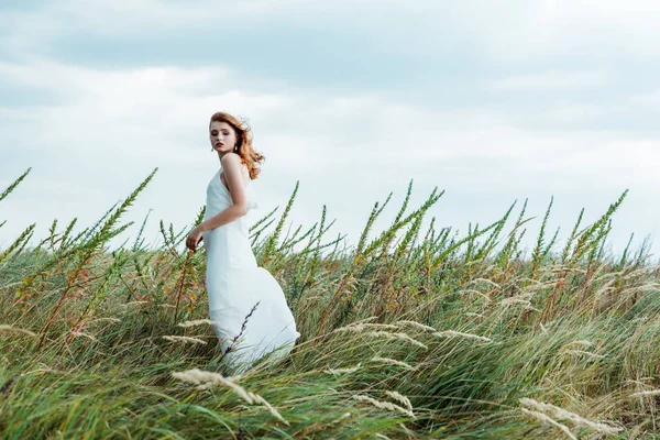 Selective focus of attractive redhead woman in white dress looking at camera — Stock Photo