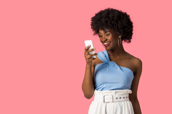 Sonriente afroamericana chica sosteniendo teléfono inteligente aislado en rosa - foto de stock