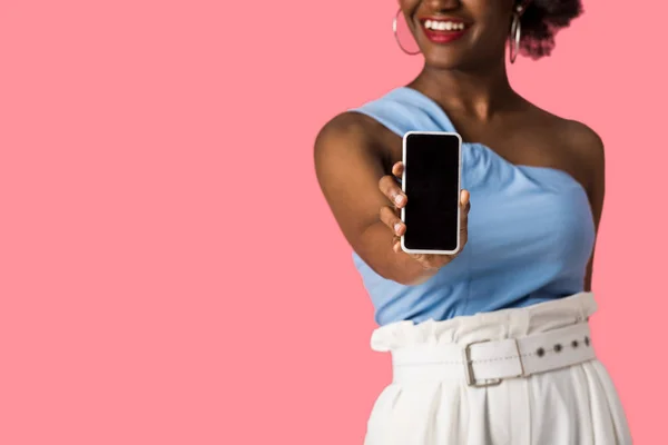 Vista recortada de la alegre chica afroamericana sosteniendo teléfono inteligente con pantalla en blanco aislado en rosa - foto de stock