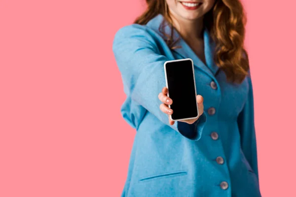 Vue recadrée de fille rousse heureuse tenant smartphone avec écran vide isolé sur rose — Photo de stock