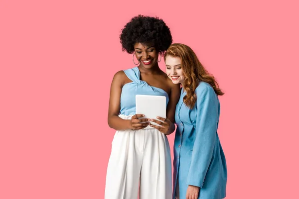 Meninas multiculturais alegres olhando para tablet digital isolado em rosa — Fotografia de Stock