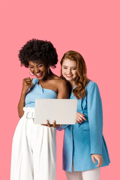 Happy multicultural girls looking at laptop isolated on pink — Stock Photo