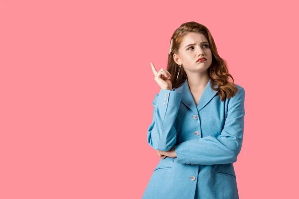 Chica pelirroja pensativa señalando con el dedo aislado en rosa - foto de stock