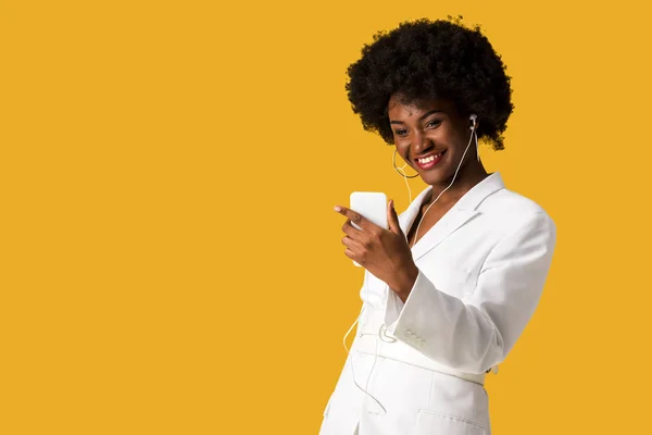 Menina americana africana feliz ouvir música enquanto segurando smartphone isolado em laranja — Fotografia de Stock