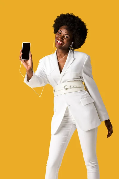 Menina americana africana alegre ouvir música enquanto segurando smartphone com tela em branco isolado na laranja — Fotografia de Stock