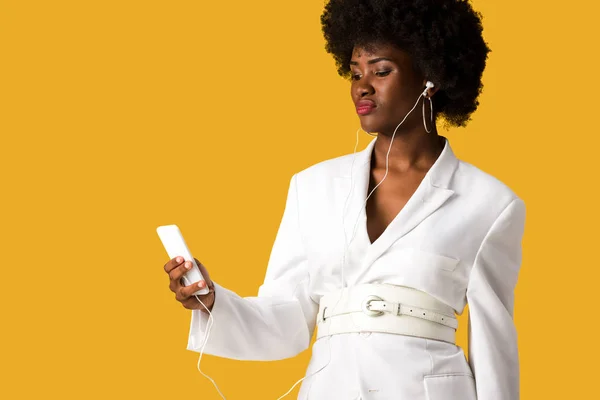 Chica afroamericana sosteniendo smartphone y escuchando música aislada en naranja - foto de stock