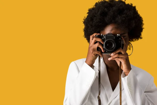 Rizado africano americano chica cubriendo la cara mientras tomando foto aislado en naranja - foto de stock