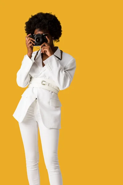 Mujer afroamericana rizada cubriendo la cara mientras toma una foto aislada en naranja - foto de stock