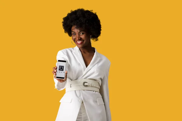 KYIV, UKRAINE - 9 de agosto de 2019: menina americana africana feliz segurando smartphone com aplicativo uber na tela isolada na laranja — Fotografia de Stock