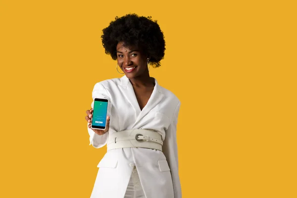 KYIV, UKRAINE - 9 AOÛT 2019 : heureuse fille afro-américaine tenant smartphone avec application twitter à l'écran isolé sur orange — Photo de stock