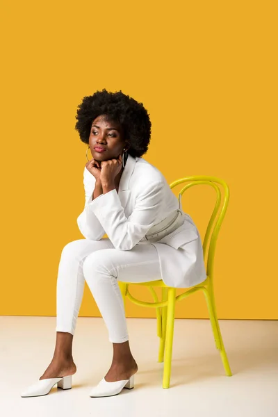 Triste afro-américaine fille assise sur chaise jaune sur orange — Photo de stock
