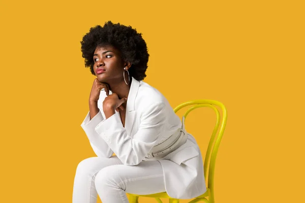 Triste afro-américaine fille assise sur chaise jaune isolé sur orange — Photo de stock