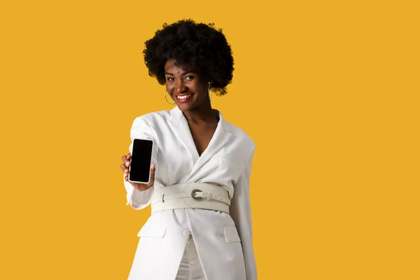 Niña afroamericana feliz sosteniendo teléfono inteligente con pantalla en blanco aislado en naranja - foto de stock