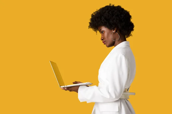 Vista lateral da menina americana africana usando laptop isolado em laranja — Fotografia de Stock