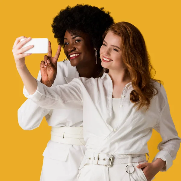 Happy multicultural girls taking selfie isolated on orange — Stock Photo