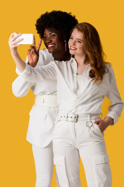 Smiling multicultural girls taking selfie isolated on orange — Stock Photo