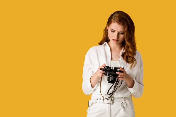 Hermosa pelirroja chica sosteniendo cámara digital aislado en naranja - foto de stock