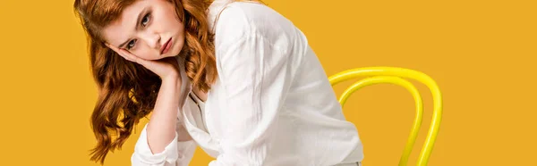 Panoramic shot of sad redhead girl sitting on chair isolated on orange — Stock Photo