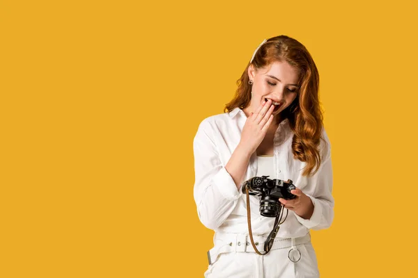 Chica pelirroja feliz sosteniendo cámara digital aislada en naranja - foto de stock