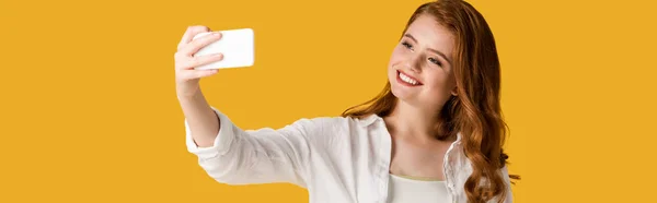 Plano panorámico de chica pelirroja feliz tomando selfie aislado en naranja - foto de stock
