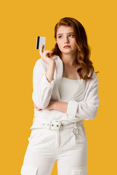 Pensive girl holding credit card isolated on orange — Stock Photo