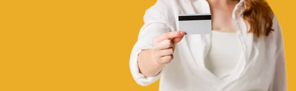 Plano panorámico de mujer joven sosteniendo tarjeta de crédito aislada en naranja - foto de stock