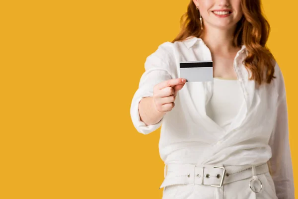 Vista ritagliata di allegra rossa ragazza in possesso di carta di credito isolato su arancione — Foto stock