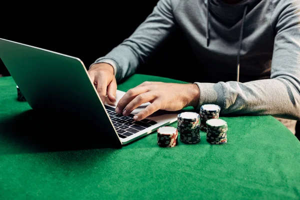 Vue recadrée de l'homme tapant sur ordinateur portable près de jetons de poker — Photo de stock
