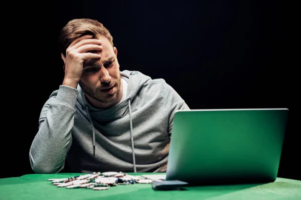 Foco seletivo de homem frustrado olhando para laptop perto de fichas de poker — Fotografia de Stock