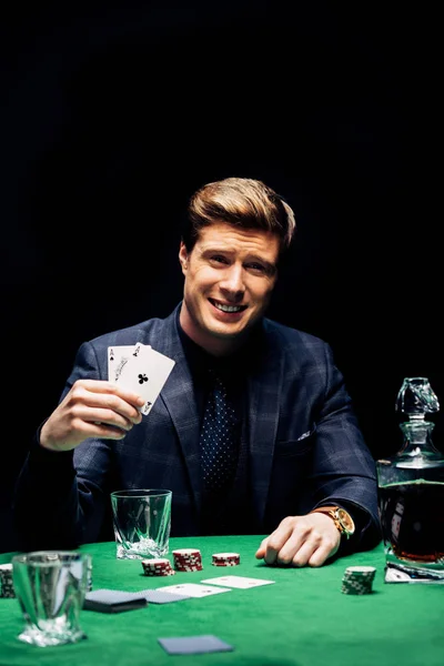 KYIV, UKRAINE - 20 AOÛT 2019 : mise au point sélective de l'homme heureux tenant des cartes à jouer et jouant au poker isolé sur noir — Photo de stock