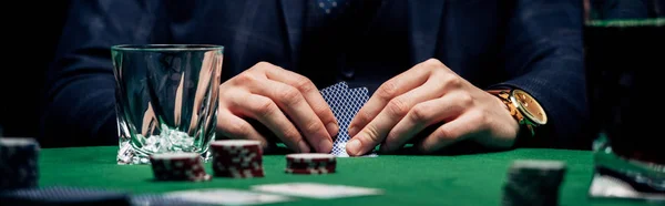 KYIV, UKRAINE - AUGUST 20, 2019: panoramic shot of man holding playing cards near glass and poker cards — Stock Photo