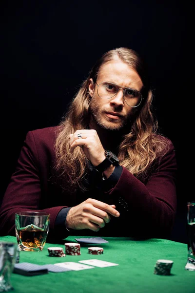 KYIV, UKRAINE - AUGUST 20, 2019: selective focus of bearded man in eye glasses near playing cards isolated on black — Stock Photo