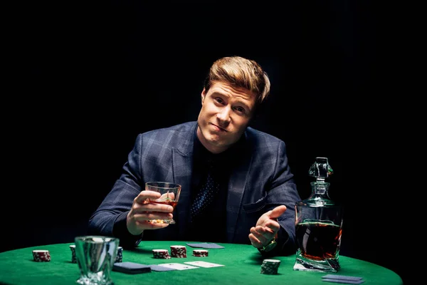 Enfoque selectivo del hombre confundido sosteniendo vidrio con whisky aislado en negro - foto de stock