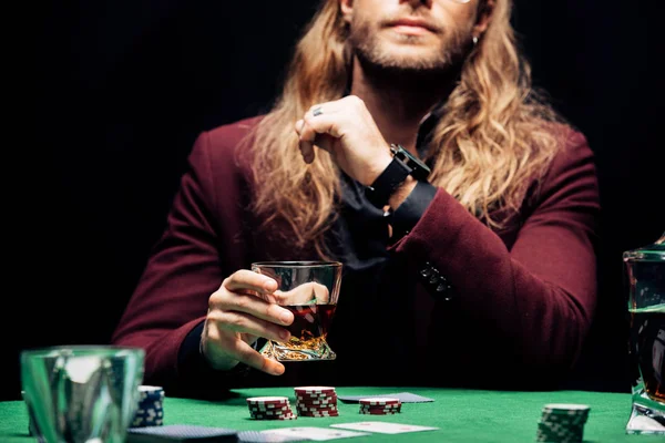 Cropped view of man holding glass with whiskey near playing cards isolated on black — Stock Photo