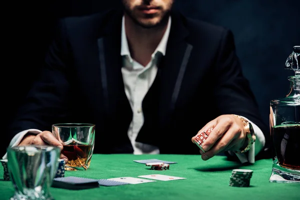 Cropped view of man holding poking chips and glass with alcohol on black with smoke — Stock Photo