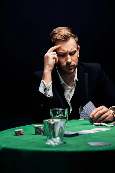 KYIV, UKRAINE - AUGUST 20, 2019: selective focus of sad man holding playing cards isolated on black — Stock Photo