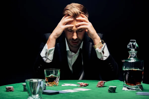 Enfoque selectivo de hombre triste sentado cerca de la mesa de póquer aislado en negro - foto de stock