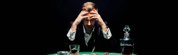 Plano panorámico de hombre triste sentado cerca de la mesa de póquer aislado en negro - foto de stock