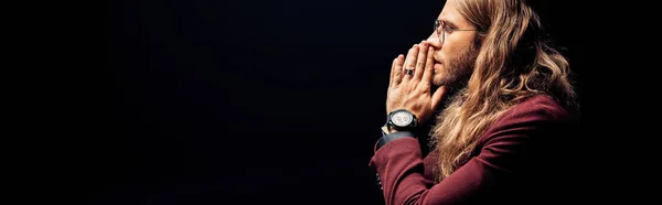 Panoramic shot of man in eye glasses with praying hands isolated on black — Stock Photo