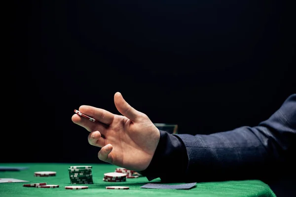 KYIV, UCRANIA - 20 de agosto de 2019: vista recortada del hombre sosteniendo la moneda de póquer mientras hace la apuesta aislada en negro - foto de stock