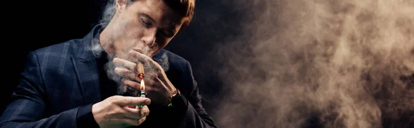 Panoramaaufnahme eines gutaussehenden Mannes mit Feuerzeug beim Rauchen auf schwarz mit Rauch — Stockfoto