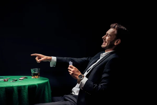 KYIV, UCRANIA - 20 de agosto de 2019: hombre feliz señalando con el dedo y sosteniendo cartas aisladas en negro — Stock Photo