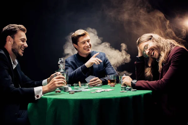 KYIV, UKRAINE - AUGUST 20, 2019: happy man pointing with finger near friends on black with smoke — Stock Photo