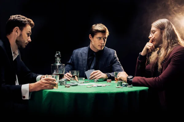 KYIV, UKRAINE - 20 AOÛT 2019 : trois amis jouant au poker sur noir avec de la fumée — Photo de stock