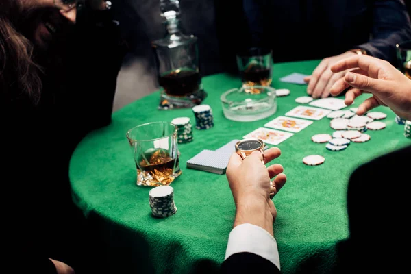 KYIV, UKRAINE - 20 de agosto de 2019: visão cortada do jogador segurando relógio enquanto joga poker no preto — Fotografia de Stock