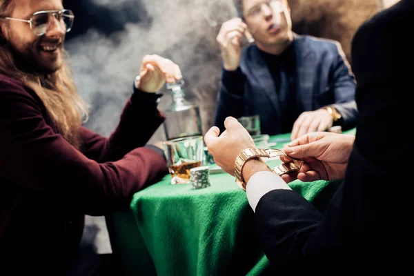 Selective focus of player holding watch while playing poker on black — Stock Photo