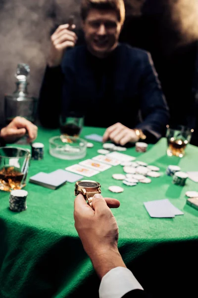 KYIV, UCRAINA - AGOSTO 20, 2019: vista ritagliata dell'uomo che tiene l'orologio mentre gioca a poker sul nero con il fumo — Foto stock