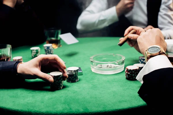 Abgeschnittene Ansicht eines Mannes, der Pokerchips in der Nähe von Croupier berührt, mit auf Schwarz isolierten Spielkarten — Stockfoto