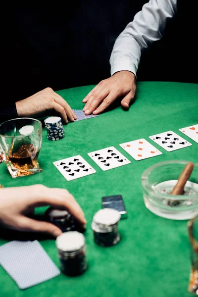 KYIV, UKRAINE - AUGUST 20, 2019: cropped view of croupier giving playing card to man isolated on black — Stock Photo